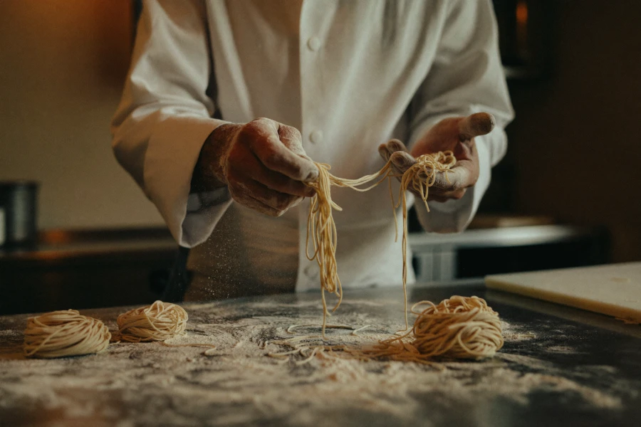 A chef's hands stretching fresh hand-made noodles.