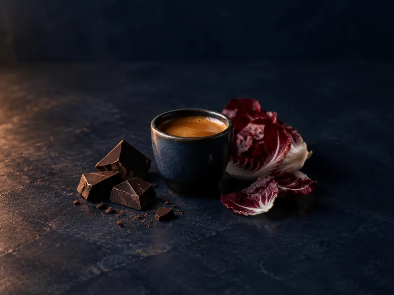 An espresso next to dark chocolate and radicchio.